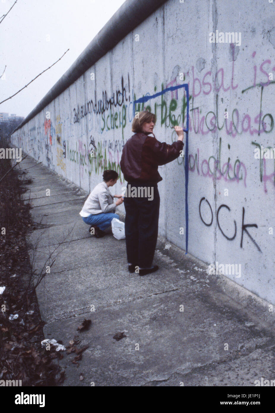 Une dame se penche sur l'appareil photo alors qu'elle peint des graffitis sur le mur de Berlin. Octobre 1987. Banque D'Images