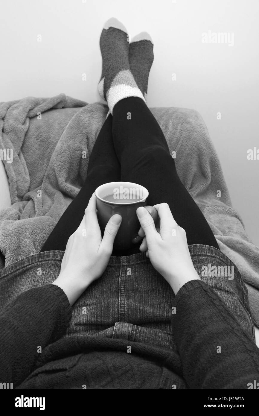 Femme tenant une tasse de café ou thé, reposant sur la table avec ses pieds jusqu'- traitement monochrome Banque D'Images