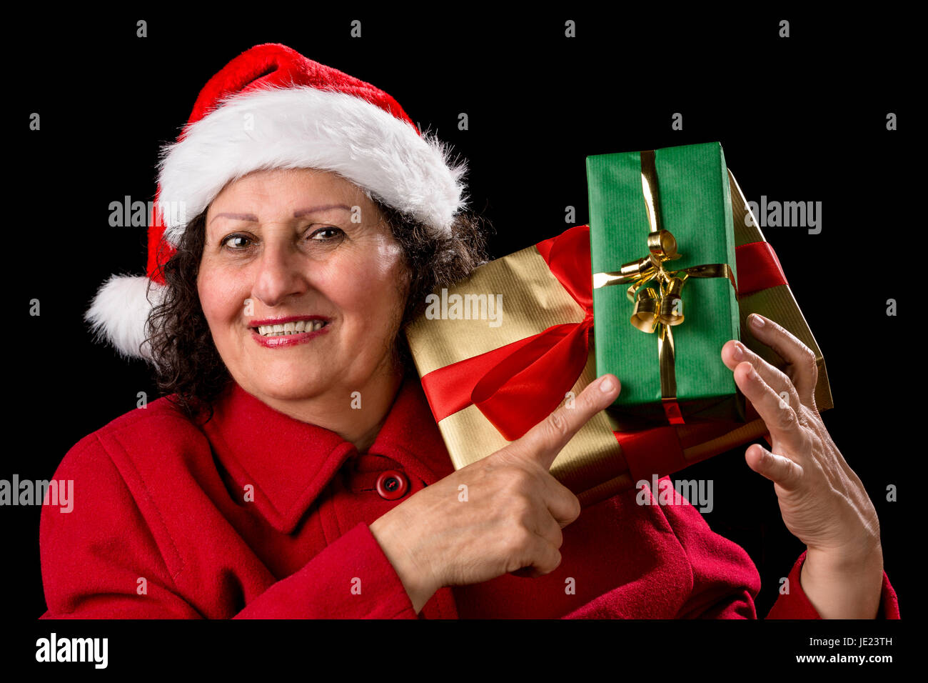 Vieille dame avec chapeau de Père Noël et manteau de velours rouge pointe avec son index droit à deux enveloppé de Noël qu'elle est en appui sur son épaule gauche. Isolé sur fond noir. Banque D'Images