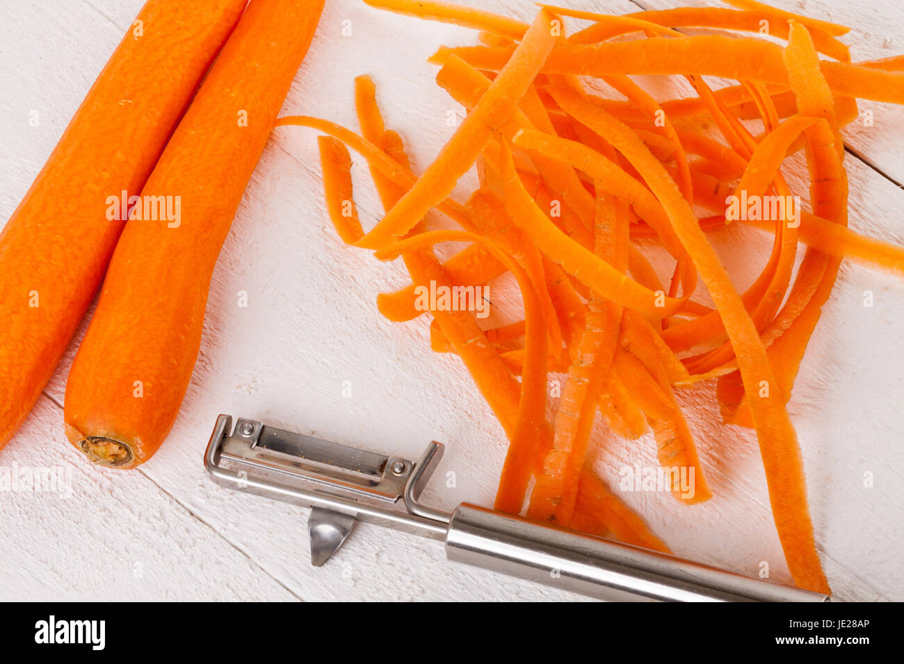 Frische orangene Karotten rüben mohrrüben geschält Sparschäler Schalen mit und auf einem Holzbrett weißer bär Banque D'Images