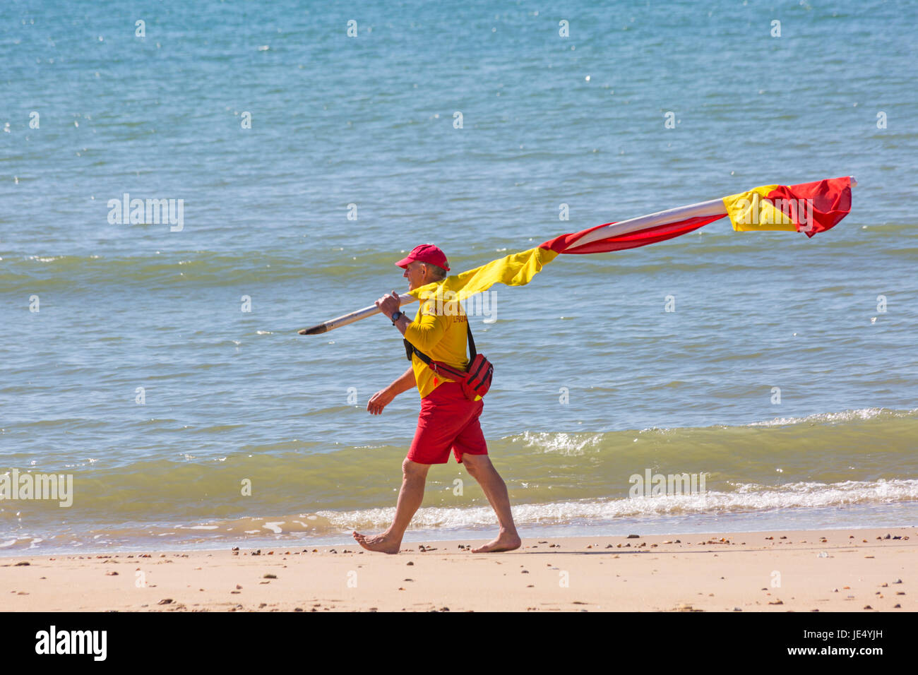 Sauveteur RNLI portant les drapeaux rouge et jaune indiquant zone sécuritaire de nager au bord de la mer, sur la plage de Bournemouth, Dorset en Juin Banque D'Images