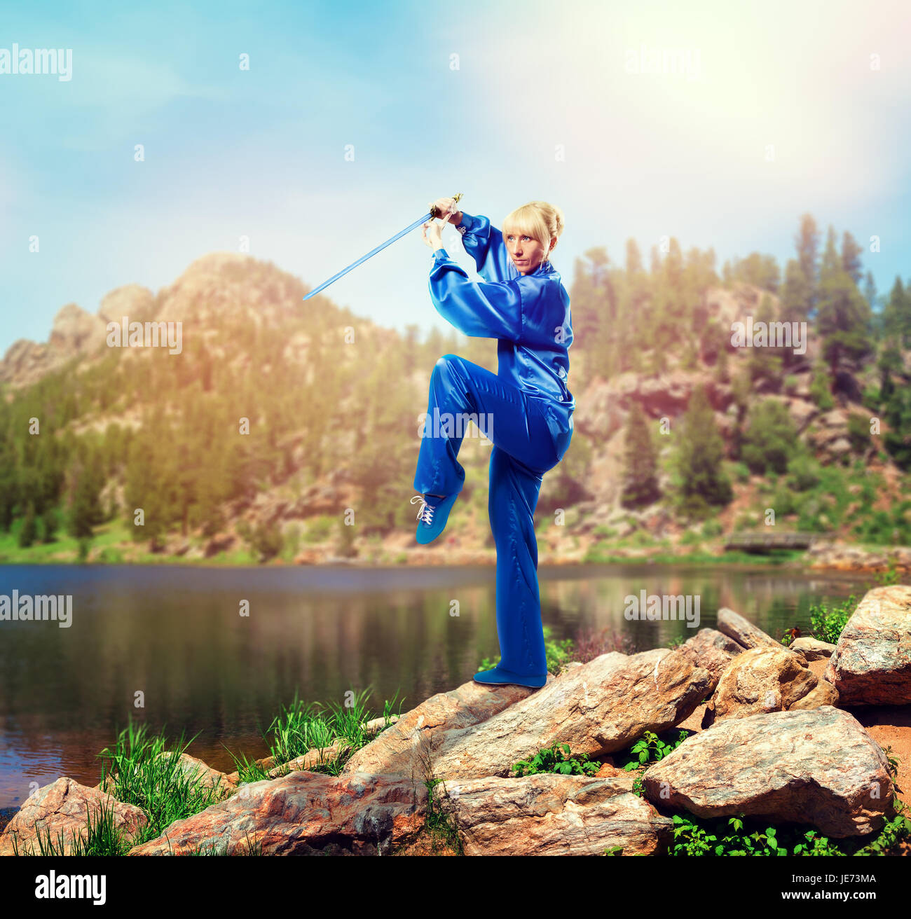 Maître de wushu femelle avec épée contre lac et montagnes, arts martiaux femme en tissu bleu sur l'entraînement au combat en plein air Banque D'Images