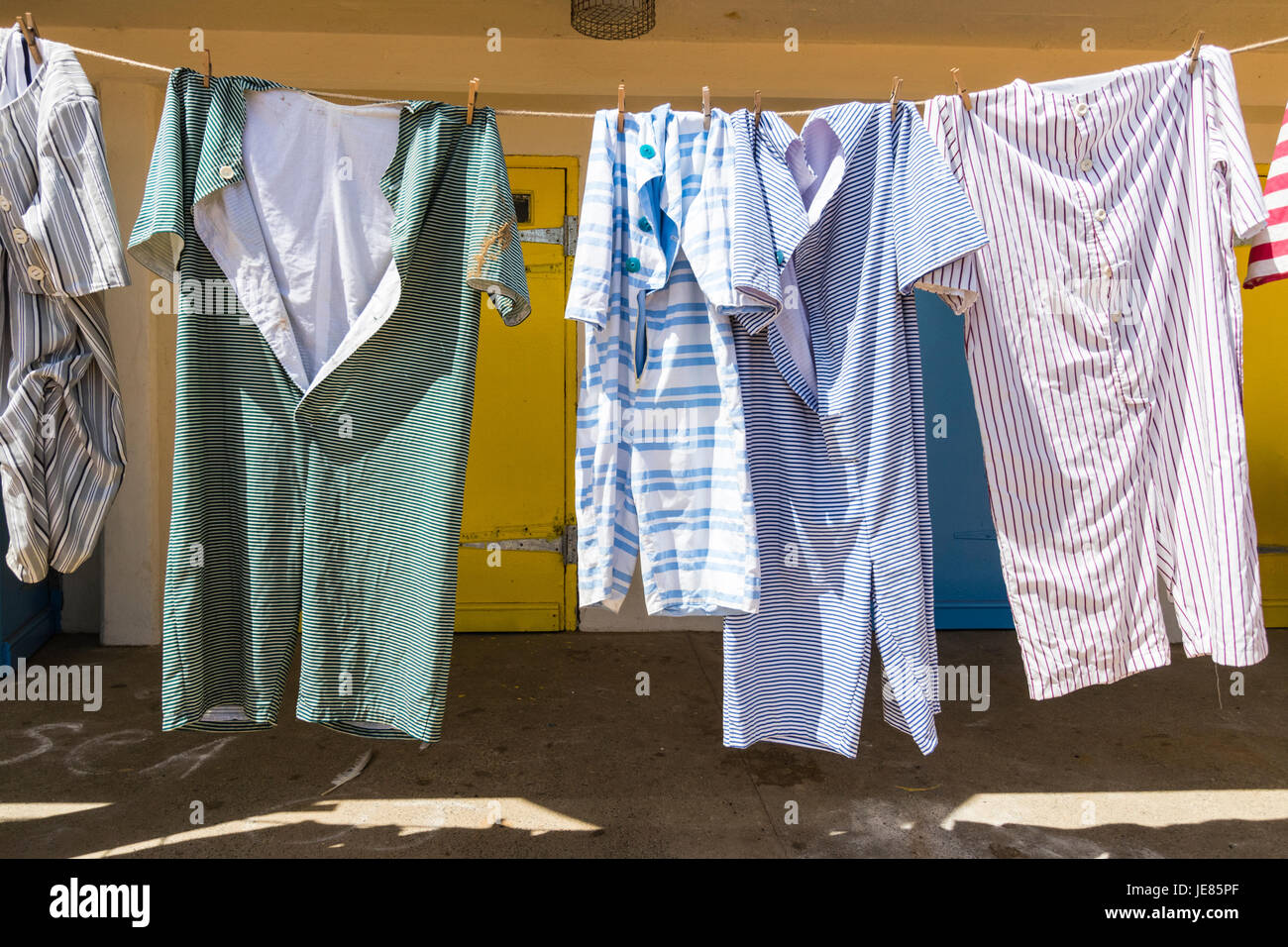 Vêtements de plage victorienne hanging on line pour sécher en face de terrasse de bleu et jaune, les portes des cabines de plage moderne de jour. Quatre costumes de bains pleine longueur. Banque D'Images