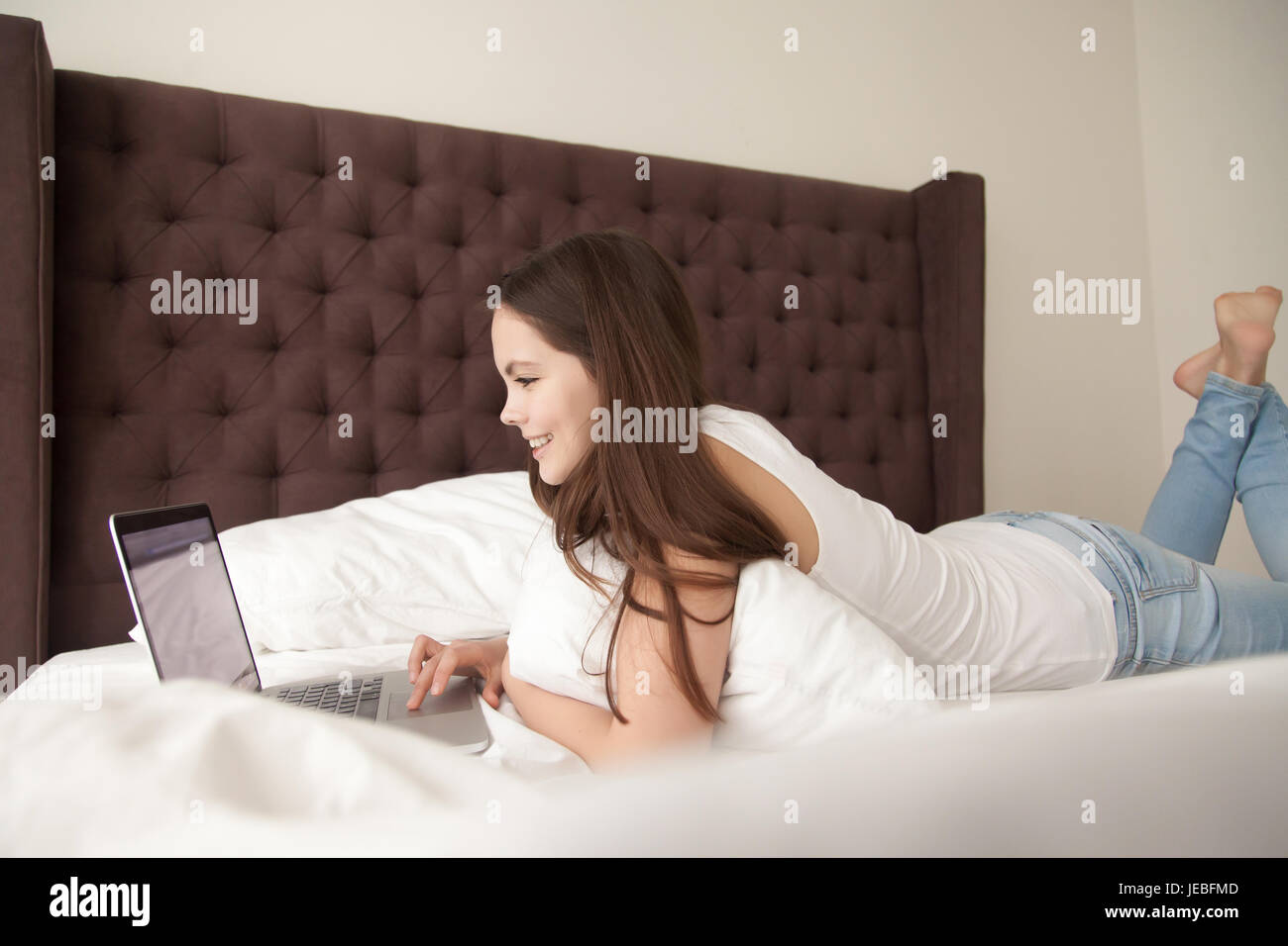 Happy young woman using laptop in bedroom Banque D'Images