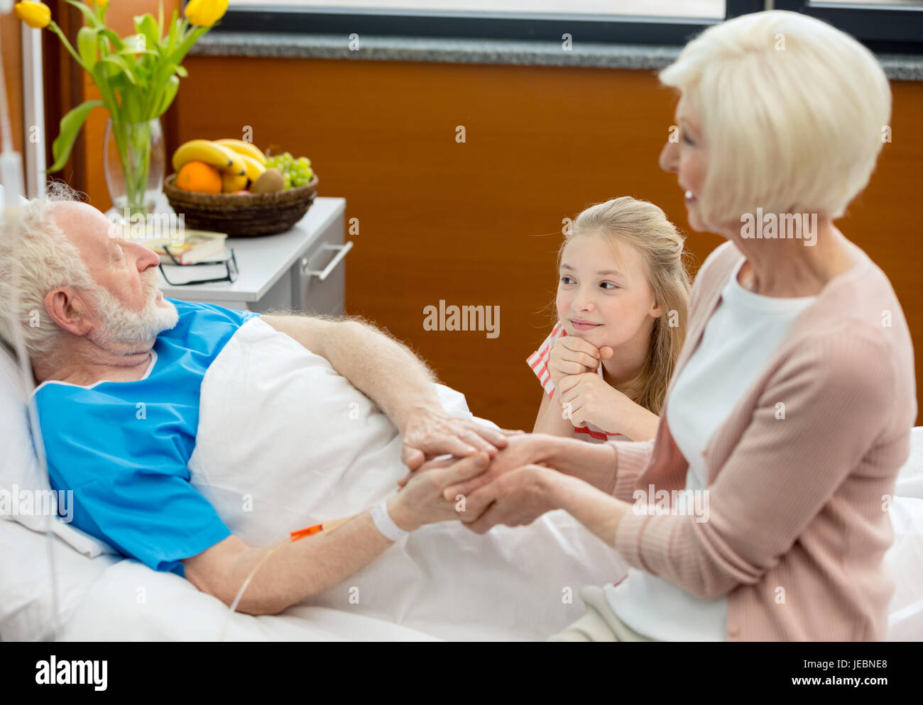 Femme et enfant visitant senior man lying in hospital bed Banque D'Images