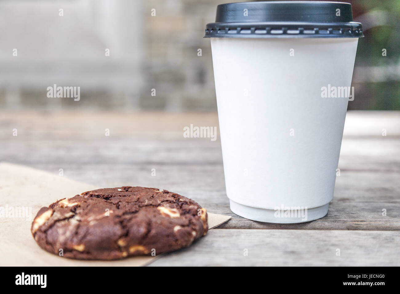 Tasse à emporter blanc avec pas de logo et d'un biscuit aux brisures de chocolat sur une table à l'extérieur Banque D'Images