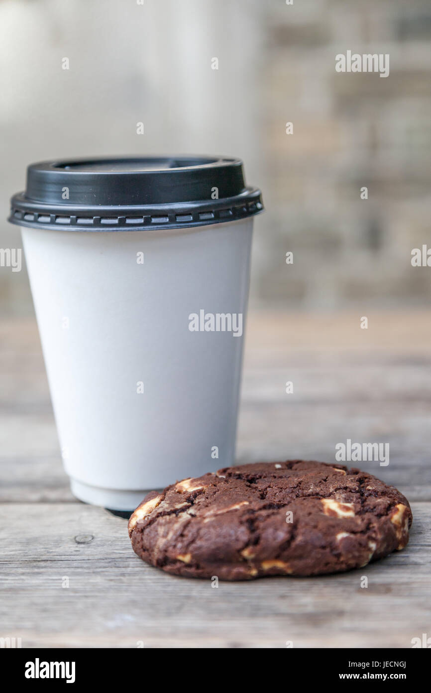 Tasse à emporter blanc avec pas de logo et d'un biscuit aux brisures de chocolat sur une table à l'extérieur Banque D'Images