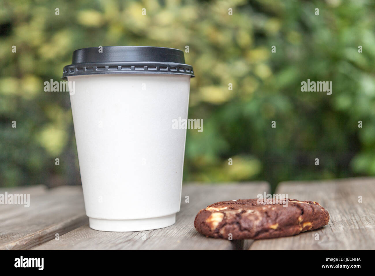 Tasse à emporter blanc avec pas de logo et d'un biscuit aux brisures de chocolat sur une table à l'extérieur Banque D'Images