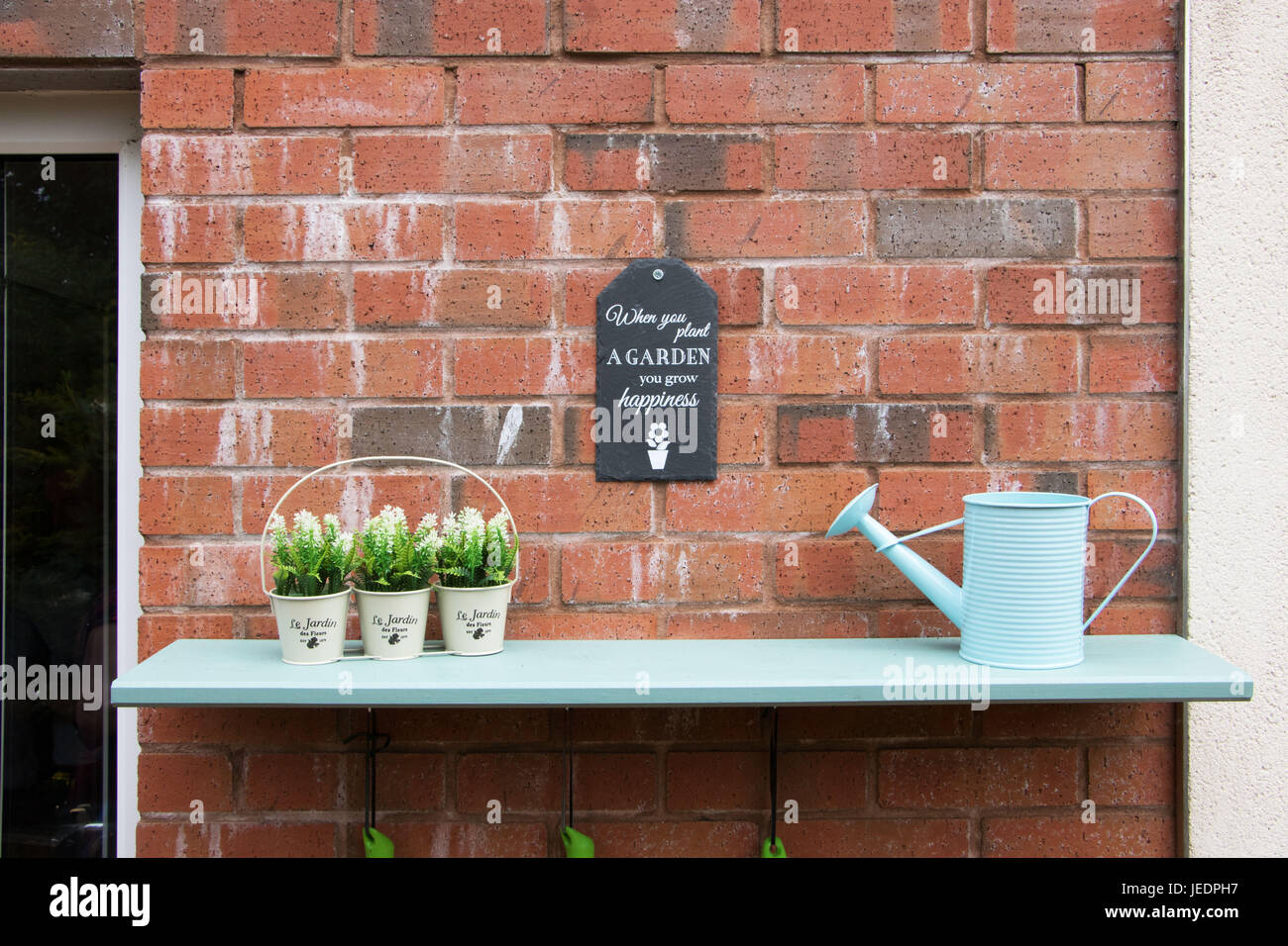 Plateau en bois peint en bleu sur un mur de briques avec des plantes et un mini arrosoir Banque D'Images