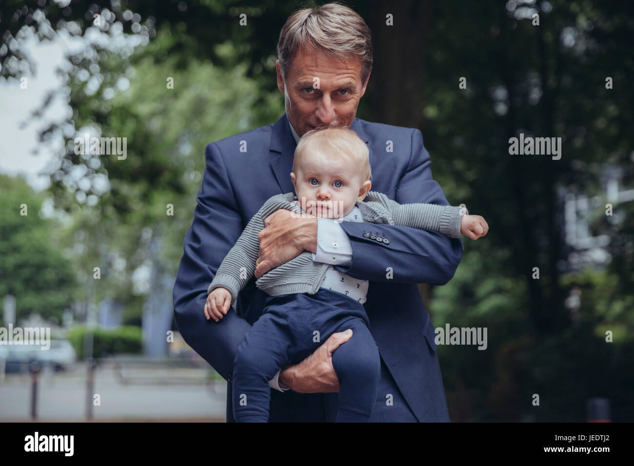 Portrait of mature businessman holding baby boy outdoors Banque D'Images