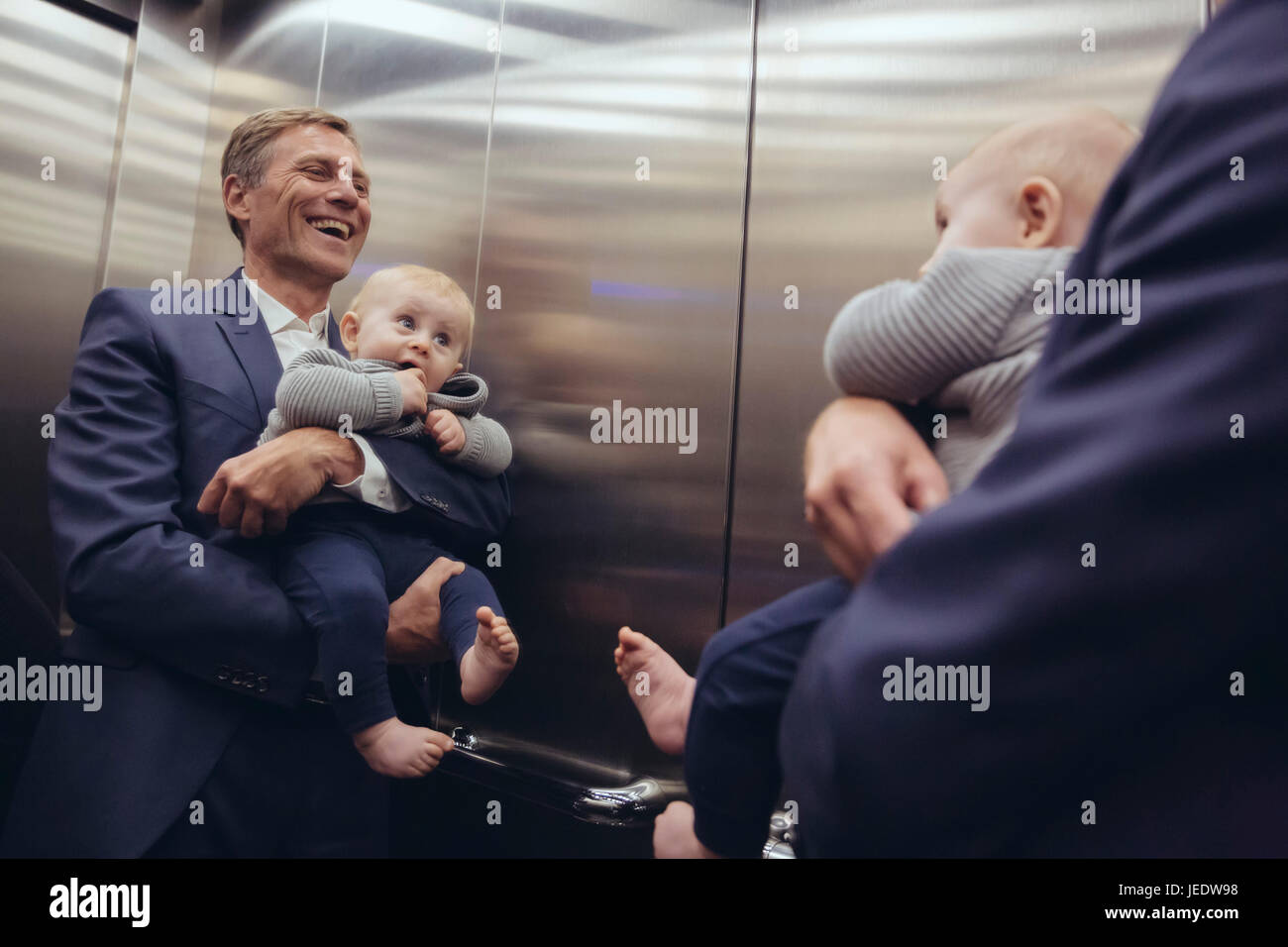 Mature businessman holding baby boy en miroir à l'ascenseur Banque D'Images