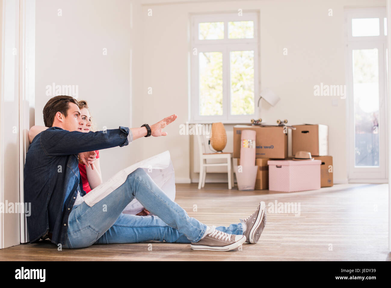 Young couple in new home sitting on floor discuter plan au sol Banque D'Images