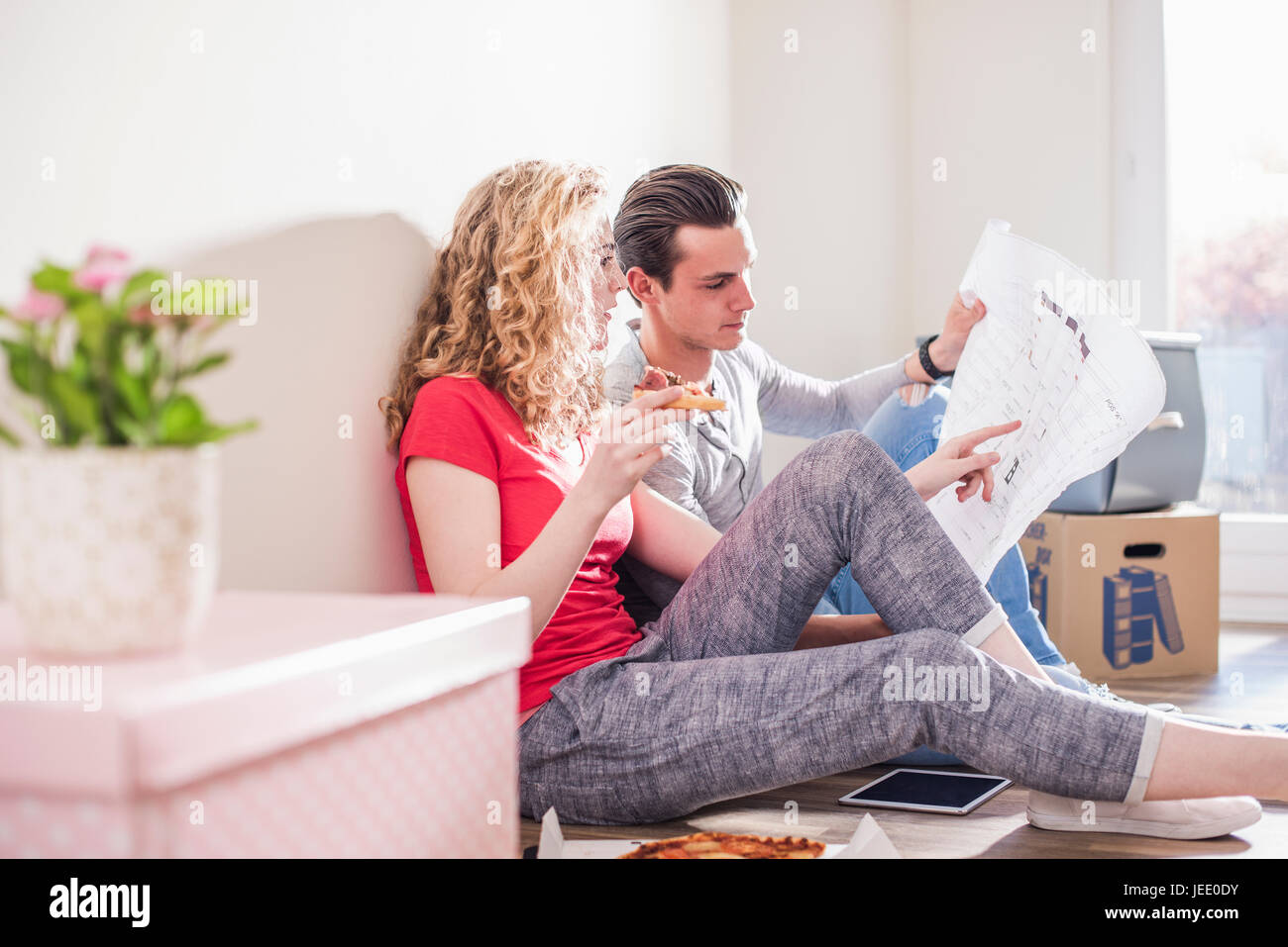 Young couple in new home sitting on floor discuter plan au sol Banque D'Images