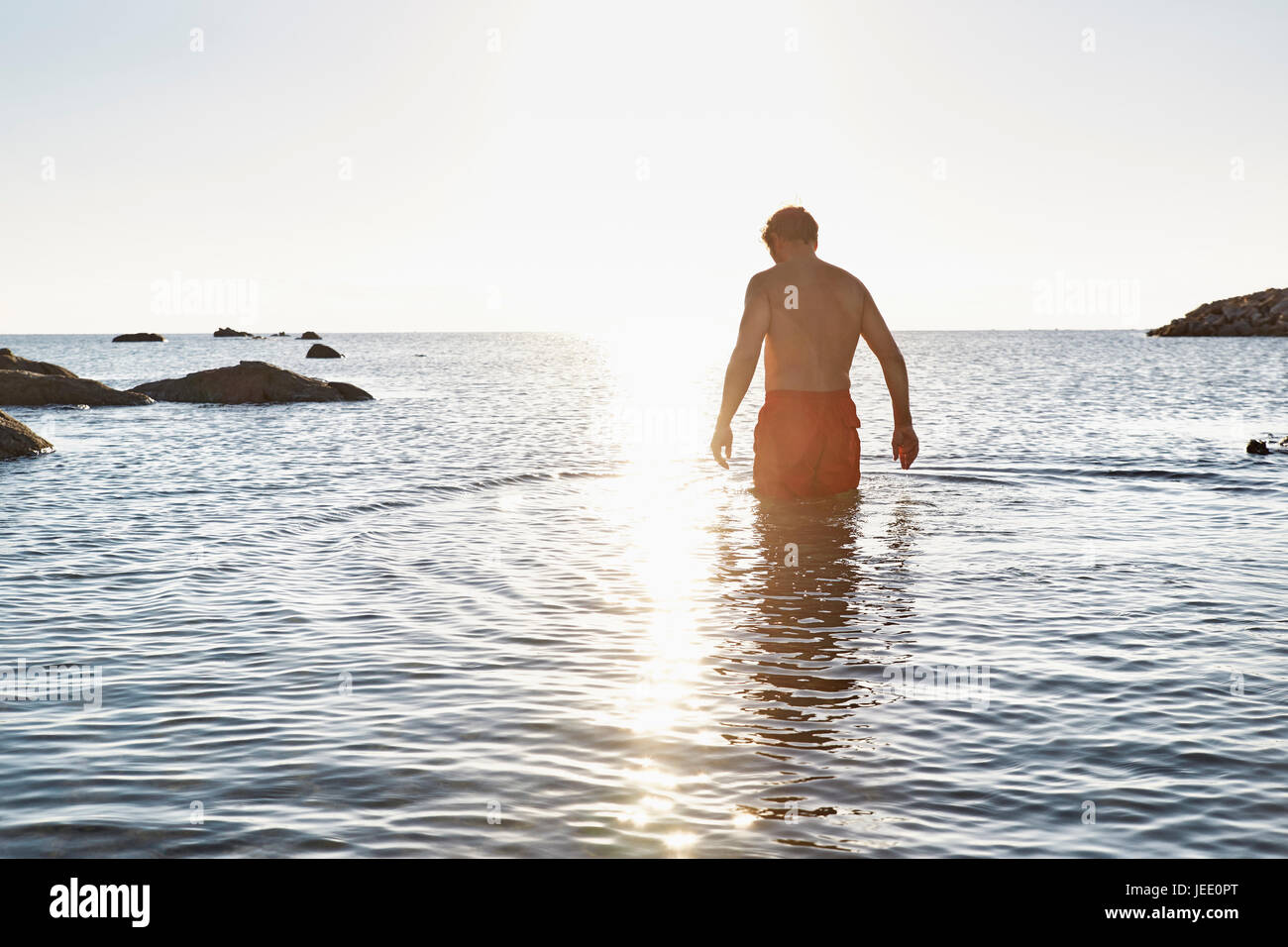 Vue arrière de l'homme debout dans la mer au coucher du soleil Banque D'Images