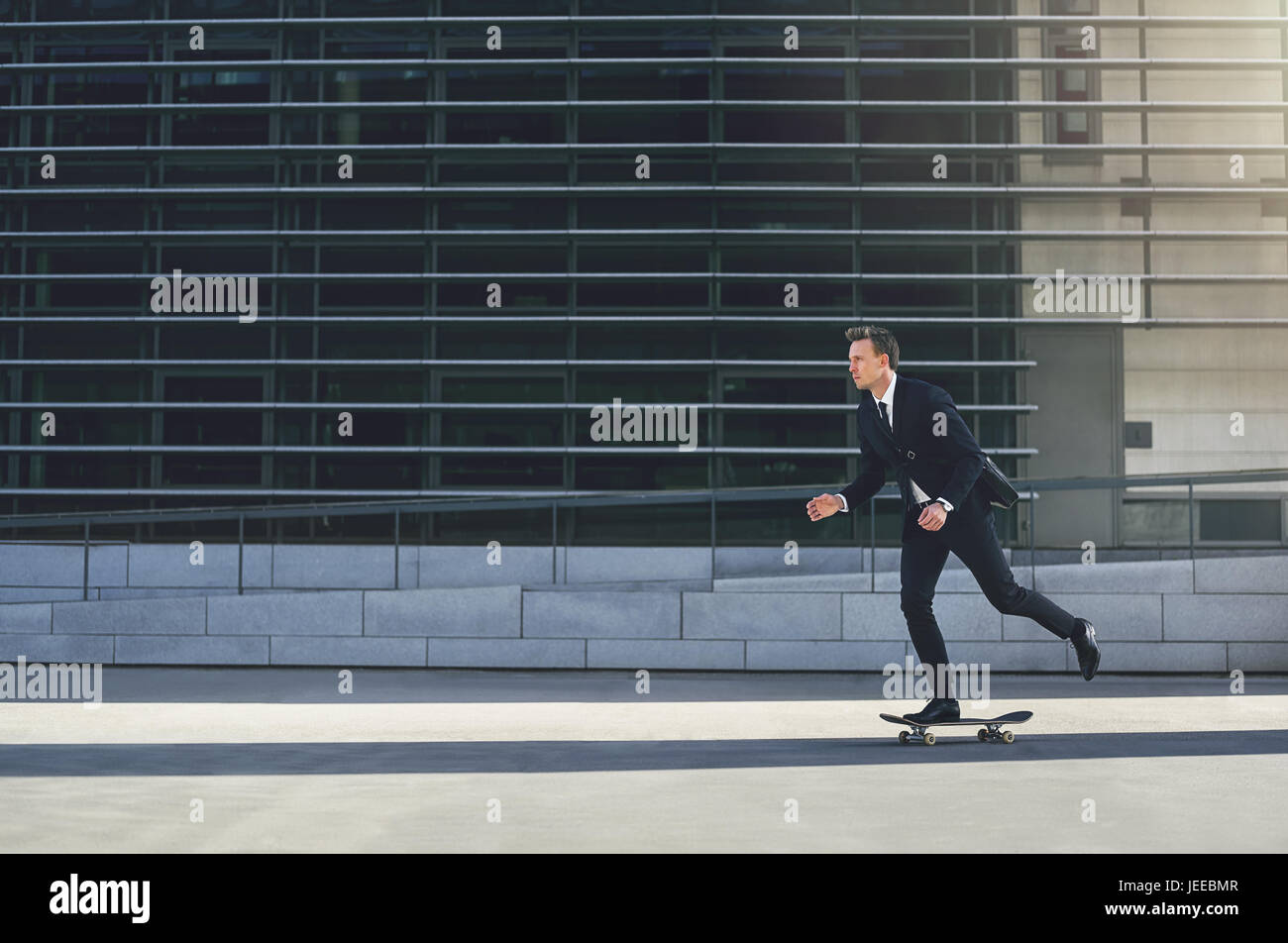 Vue latérale d'un jeune businessman riding skateboard dans la ville. Banque D'Images