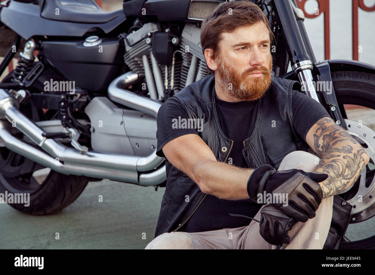 Barbe rousse barbus avec des motards en blouson de cuir assis sur le plancher près de vélo. Banque D'Images