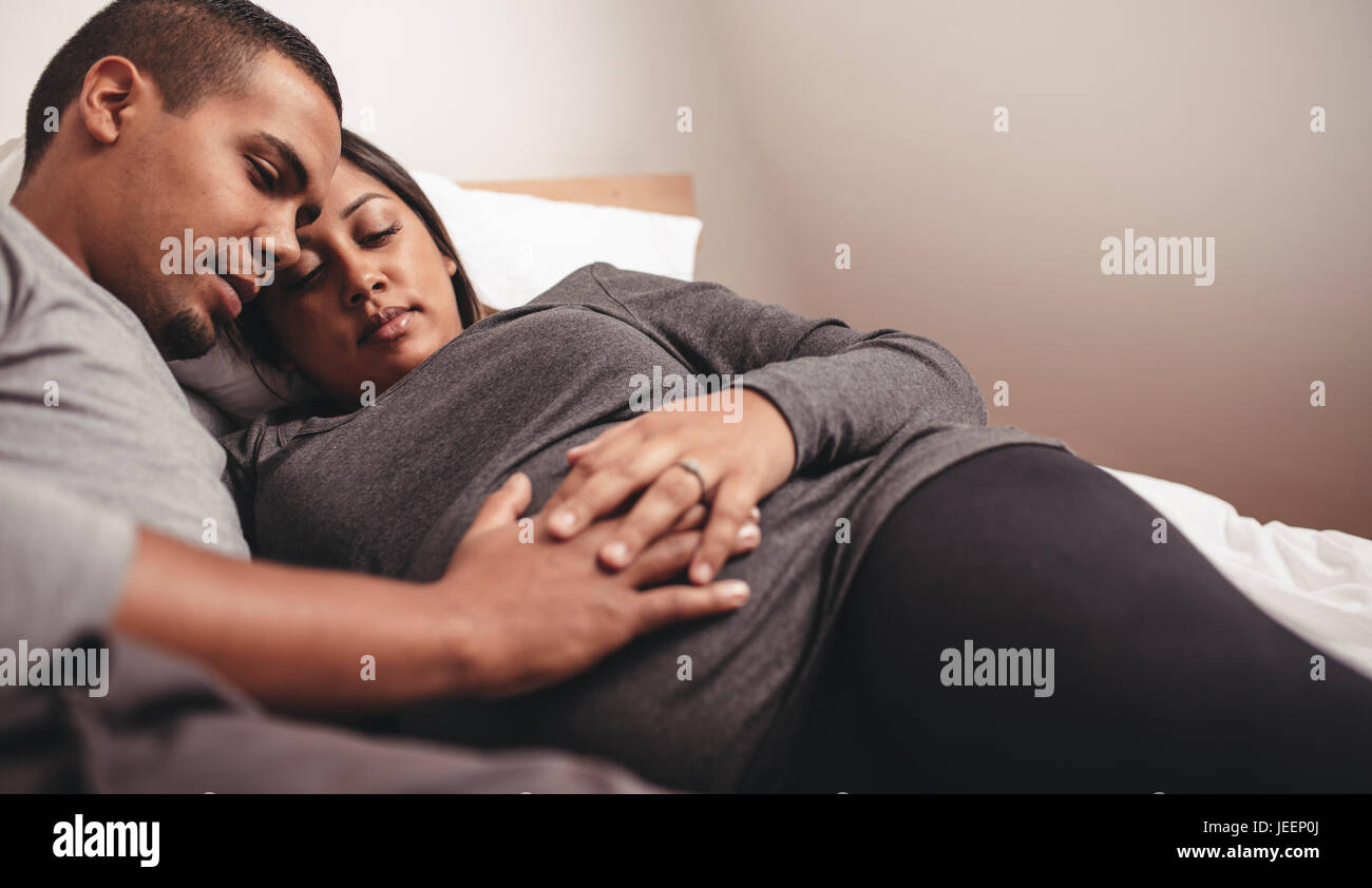 African man and woman lying on bed avec leurs mains sur le ventre. Jeune couple aimant attend bébé. Banque D'Images