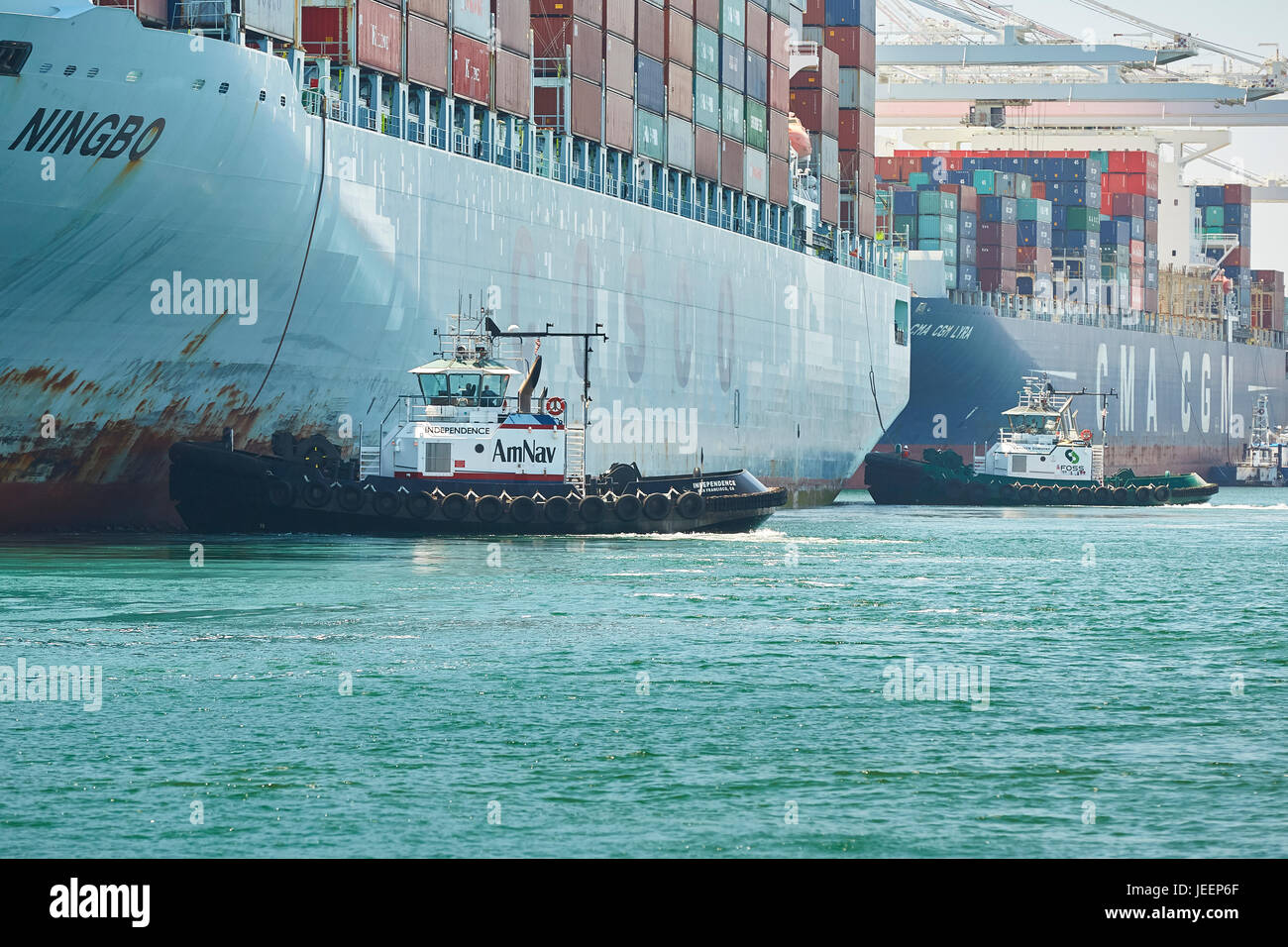 Le porte-conteneurs COSCO Géant Ningbo est guidée dans Quai J270 sur Pier J par deux remorqueurs du tracteur au terminal à conteneurs de Long Beach, Los Angeles, USA. Banque D'Images