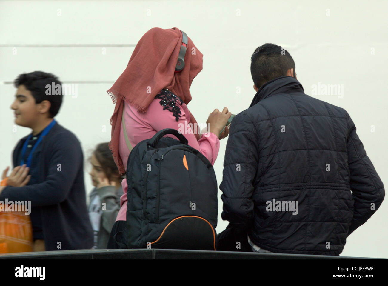 La famille asiatique vêtue de réfugiés foulard Hijab sur street au Royaume-Uni scène quotidienne couple jeune fille casque sur l'écharpe d'écouter de la musique Banque D'Images