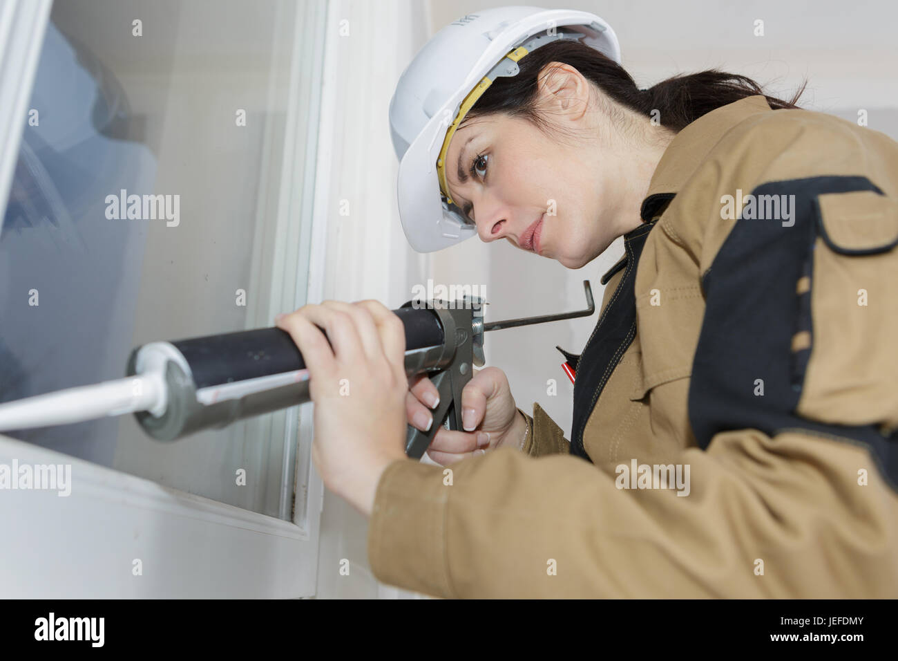 Le renouvellement d'un travailleur féminin joint silicone sur une fenêtre Banque D'Images