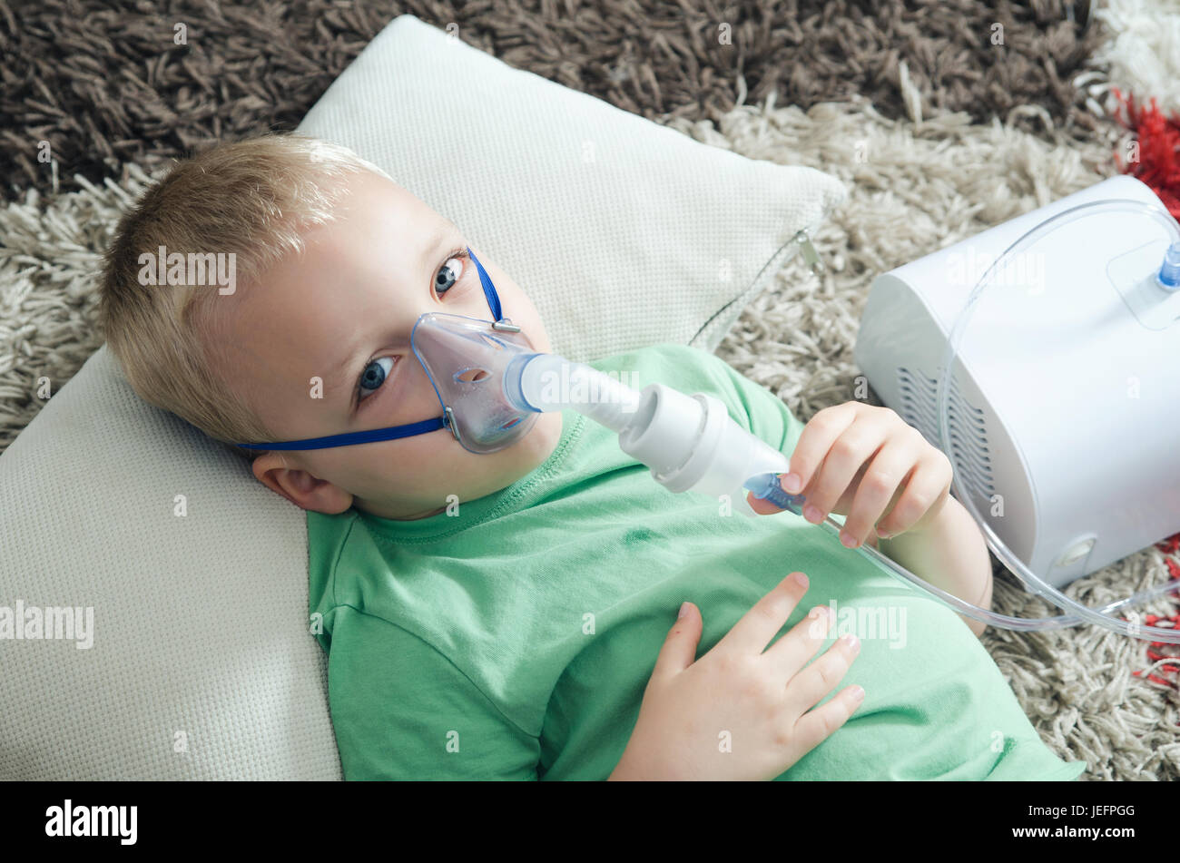 petit garçon malade avec inhalateur pour le traitement de la toux. enfant  malade faisant de l'inhalation sur son lit. saison de la grippe.  intervention médicale à domicile. intérieur et vêtements aux couleurs
