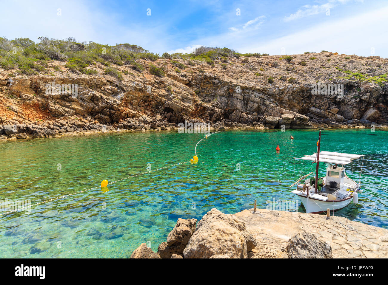 Bateau de pêche typique blanc magnifique mouillage dans la baie de Cala Carbo avec de l'eau de mer vert émeraude, l'île d'Ibiza, Espagne Banque D'Images