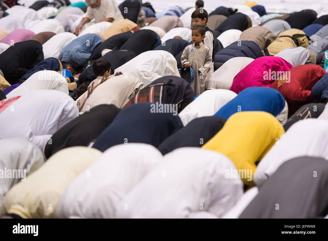 Un enfant observe alors que les hommes prennent part à des prières au cours de l'Eid dans Excel, l'événement en association avec la Fondation Al-Khair à ExCeL, Londres, qui est la plus grande célébration de l'aïd de Londres. Banque D'Images