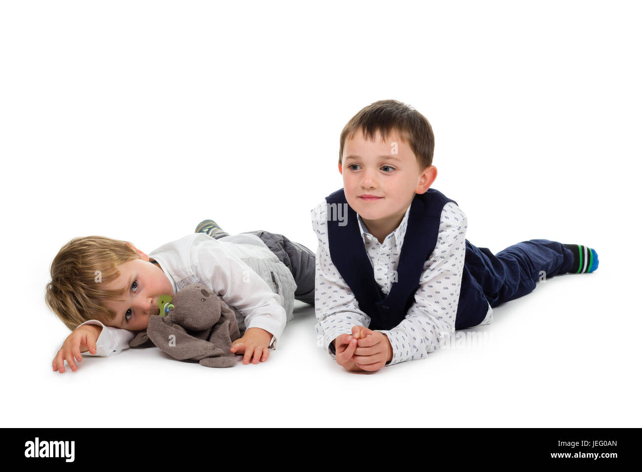 2 Petits frères portant des vêtements de fête, allongé sur le sol, avec des animaux en peluche (lapin) et sucette. Isolé sur fond blanc Banque D'Images