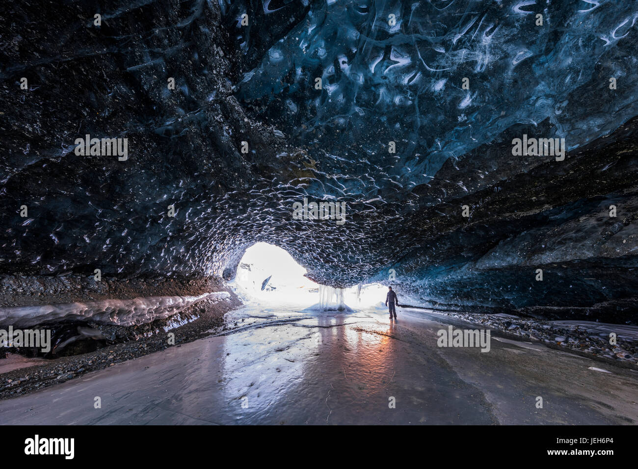 Un homme se tient près de l'entrée d'un tunnel sous la glace de glacier Canwell aux couleurs du coucher du soleil qui se reflète sur la glace au milieu de l'hiver Banque D'Images