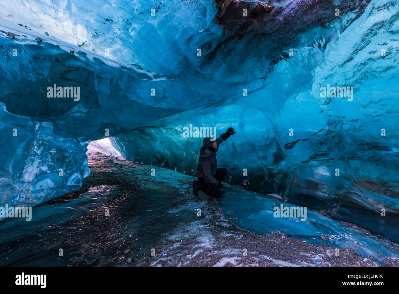 Un homme examine la glace bleue claire à l'intérieur d'un tunnel sous la surface de Black Rapids Glacier en hiver ; Alaska, États-Unis d'Amérique Banque D'Images