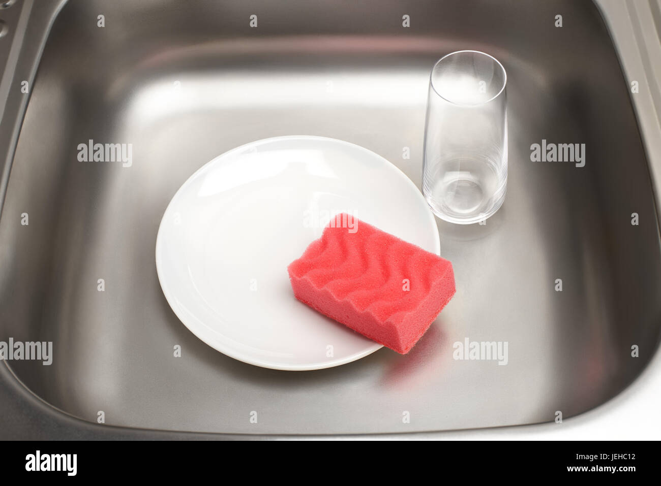 Close up d'évier de cuisine avec plaque blanche et rose, éponge de nettoyage et verre Banque D'Images