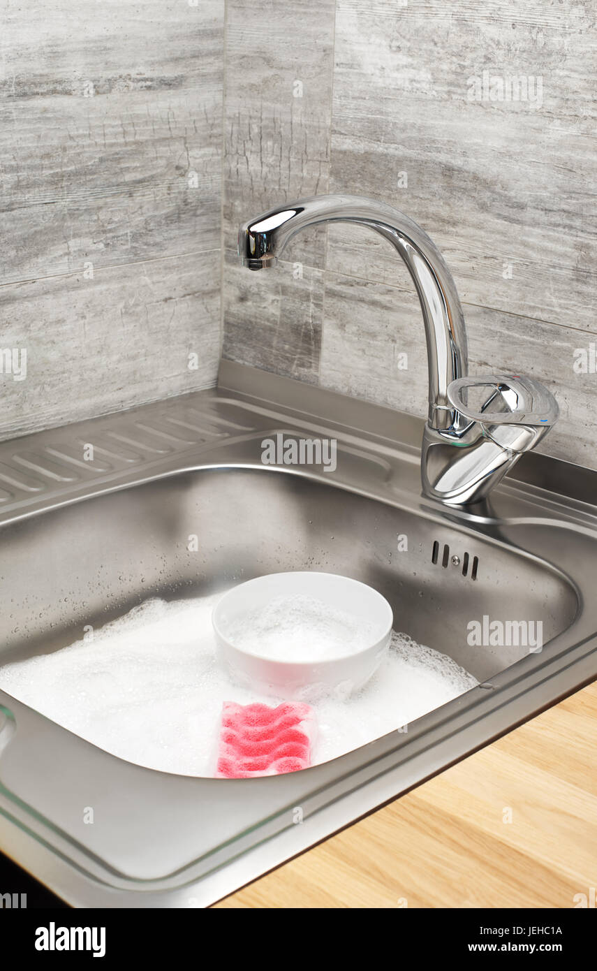 Close up d'évier de cuisine pleine de mousse, de la table et rose éponge de nettoyage Banque D'Images