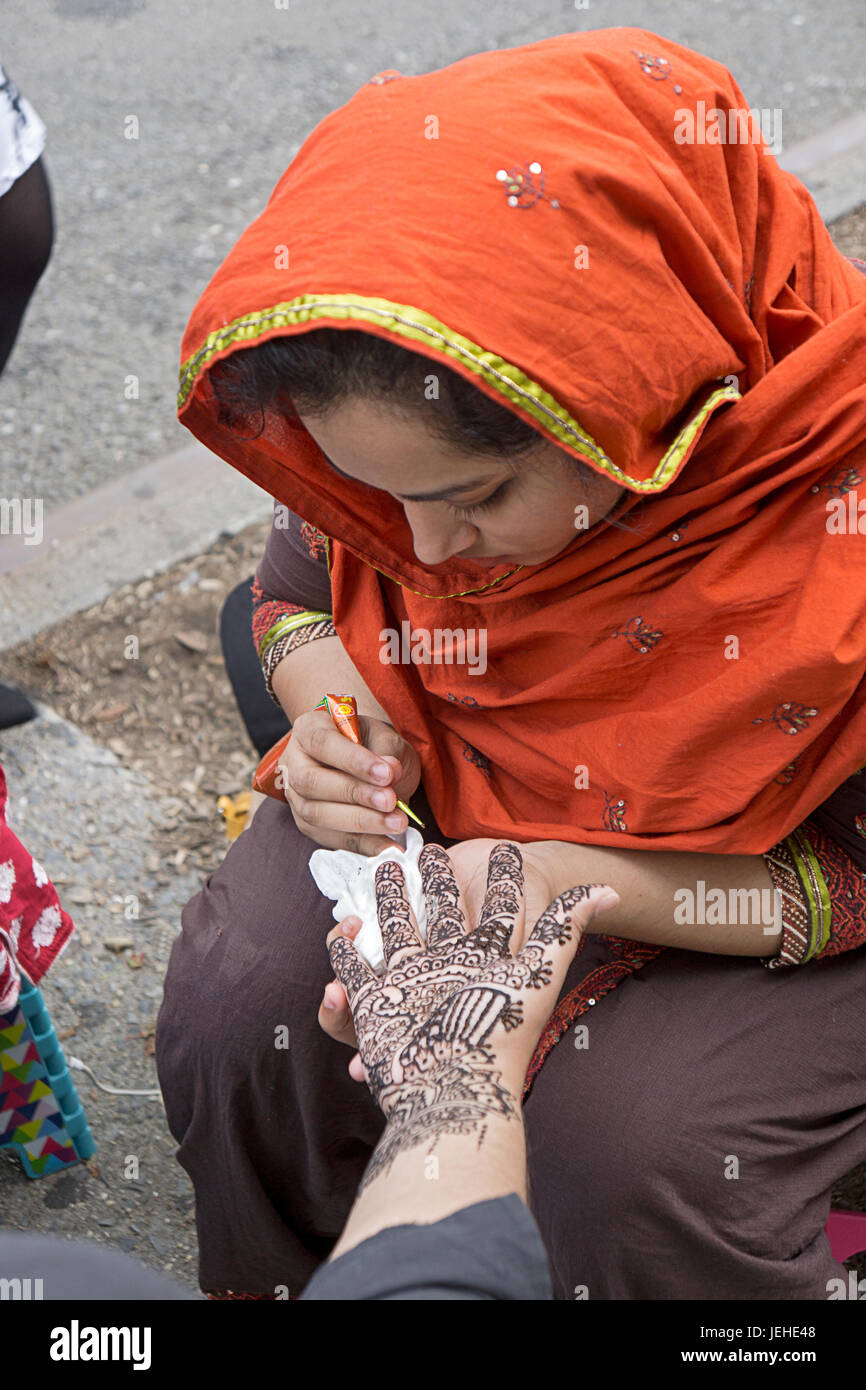 Une femme musulmane en costume traditionnel décore une femme avec la main de henné pour célébrer l'Aïd Al Fitr marquant la fin du Ramadan. Queens, New York. Banque D'Images