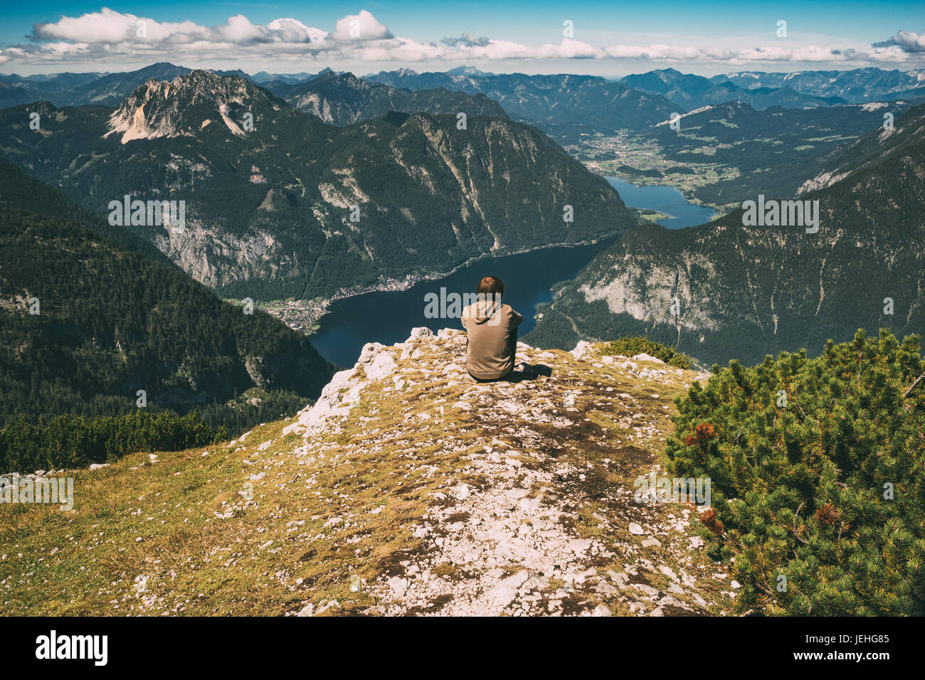 Jeune homme assis sur le bord de la montagne et bénéficiant d'une vue spectaculaire. Image aux tons Vintage Banque D'Images