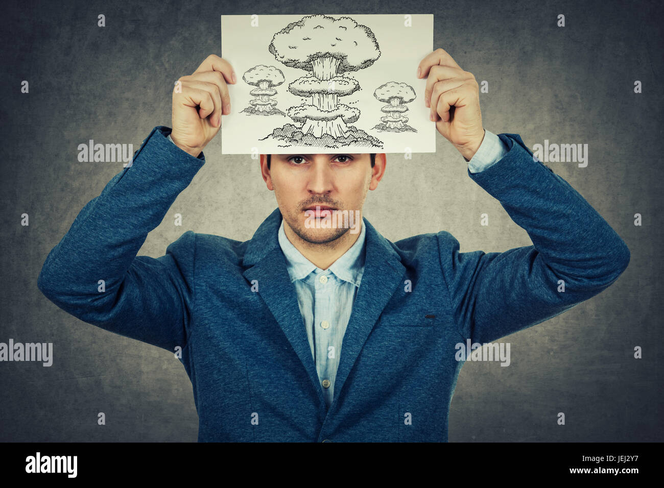 Young businessman holding a white paper sur sa tête avec un dessin d'explosion , isolé sur fond de mur gris.L'état mental de la dépression. Banque D'Images