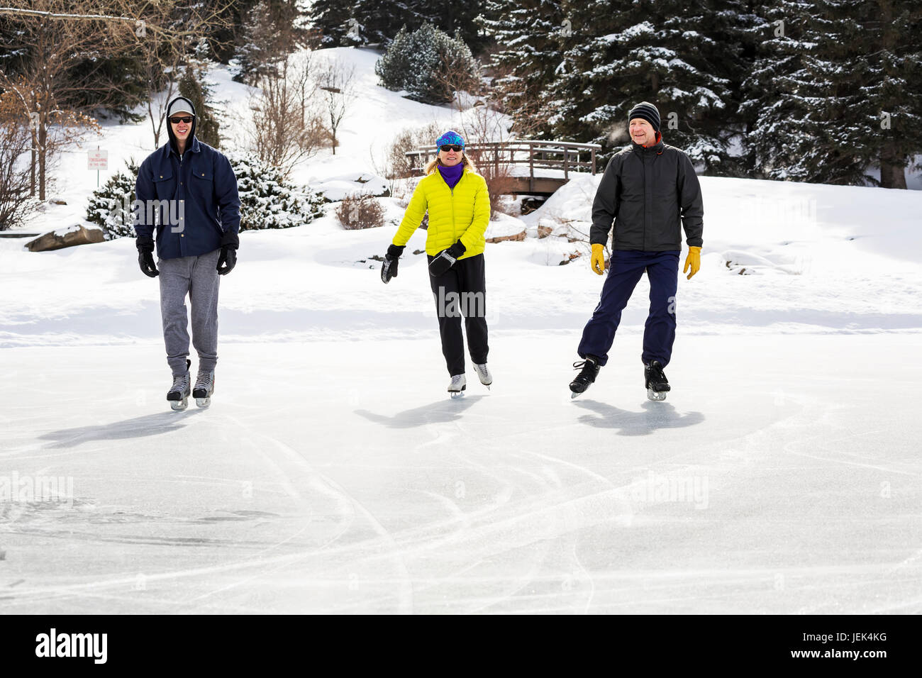 Deux hommes et une femme patinage sur l'étang avec des pont couvert de neige dans l'arrière-plan ; Calgary, Alberta, Canada Banque D'Images