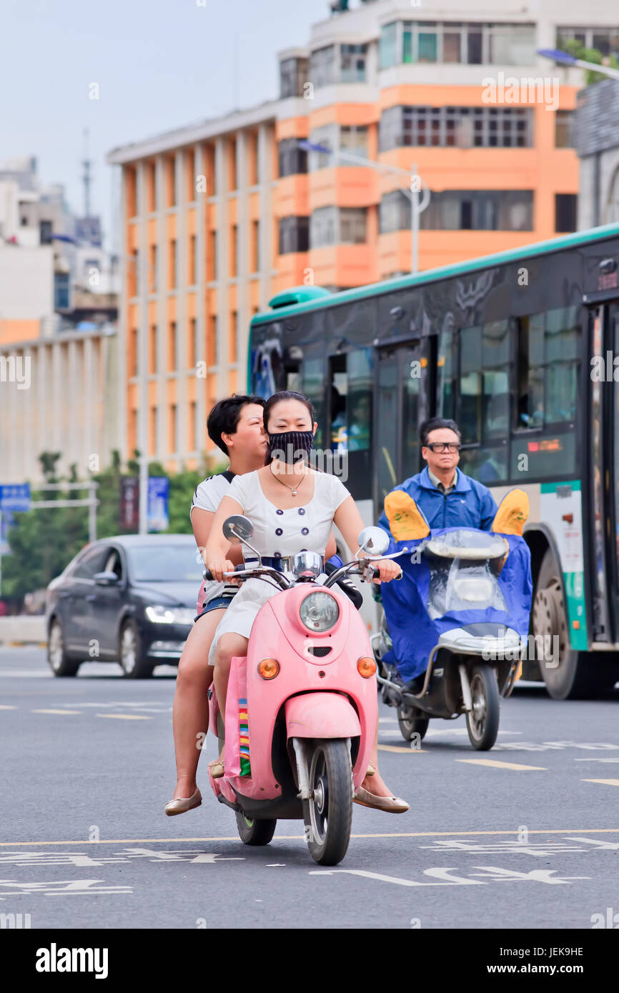 KUNMING-30 JUIN 2014. Fille avec bouchon de bouche sur e-vélo. Un nombre croissant de citoyens chinois portent une protection respiratoire contre la pollution atmosphérique. Banque D'Images
