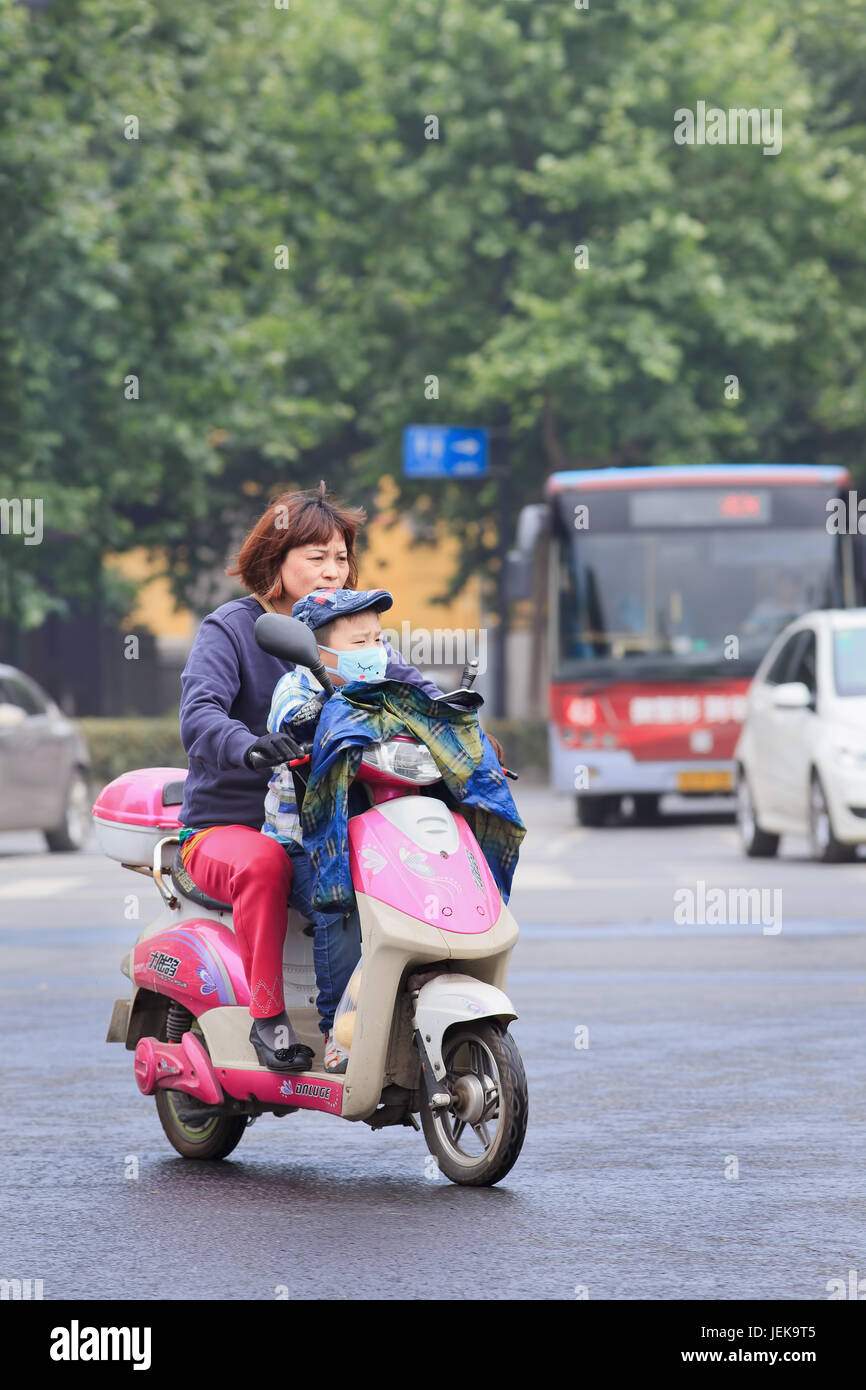 NANJING-LE 25 MAI 2014. Femme sur e-bike avec enfant portant protection respiratoire. Le nombre croissant de Chinois portent une protection respiratoire contre la pollution. Banque D'Images