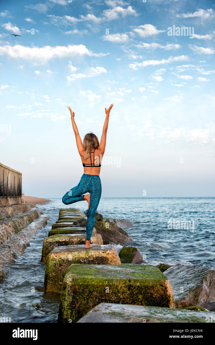 Woman practicing yoga par le comité permanent de la mer sur les roches Banque D'Images