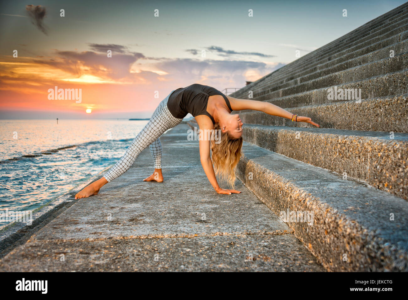Woman doing yoga au coucher du soleil par la mer Banque D'Images