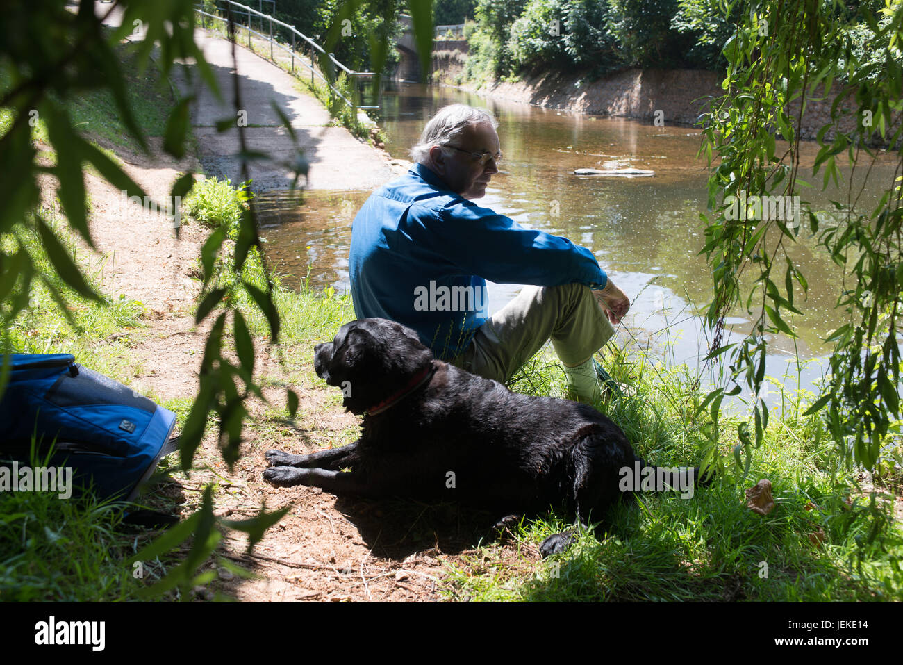 Par Guy Pic Newman. 15.07.2013. Scène paisible - un elederly gentleman prend une pause avec son fidèle chien assis près de la rivière, Sid, Cornwall, Devon. Banque D'Images