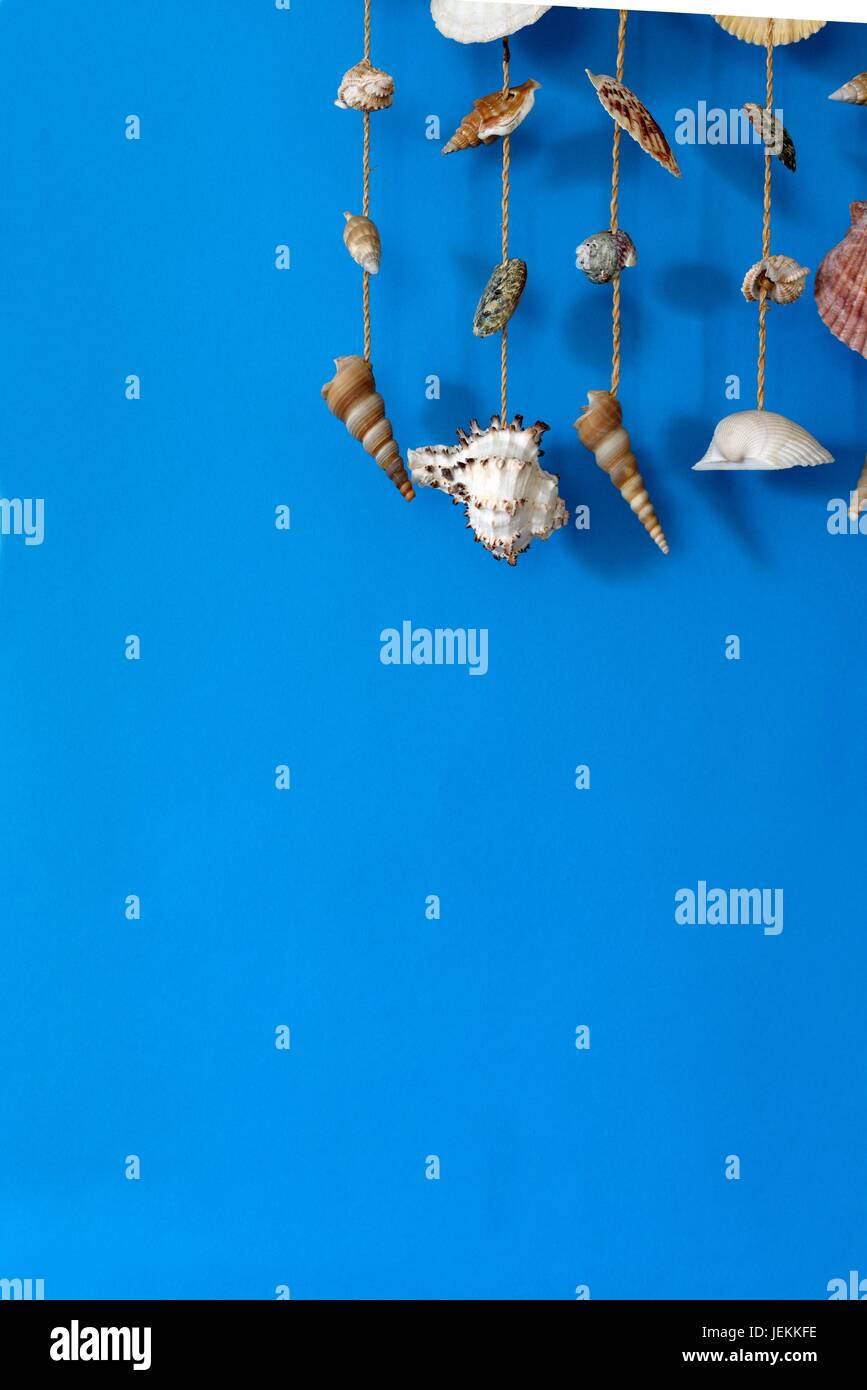 Un carillon à vent avec des coquillages sur fond bleu sur un bâton Banque D'Images