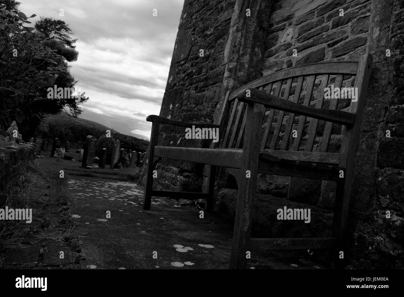 L'extérieur du banc solitaire vieille église campagne donnant sur un cimetière. Banque D'Images