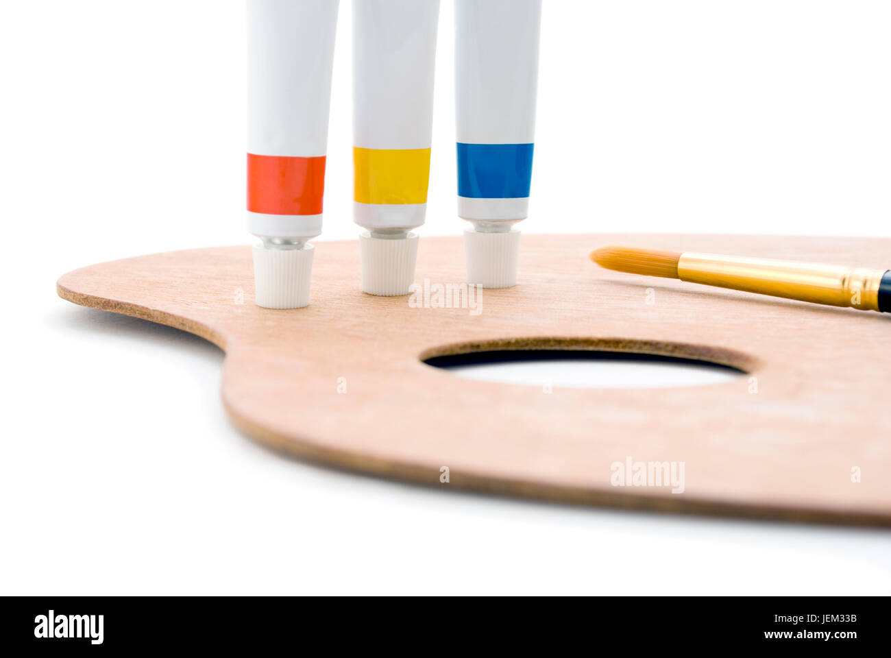 Trois tubes de peinture (couleurs primaires) debout sur le bord de la palette en bois avec trou de pouce et la pointe de pinceau visible. Libre shot, recadré à huis clos Banque D'Images