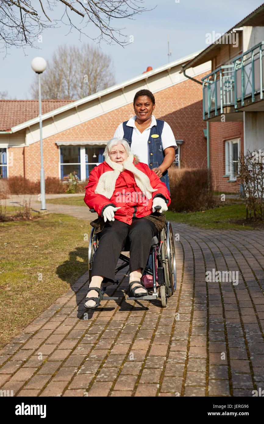 Infirmière de marcher avec senior woman sur fauteuil roulant Banque D'Images