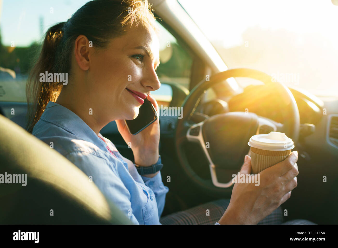 Young businesswoman talking on un smartphone et de boire du café tout en conduisant une voiture Banque D'Images