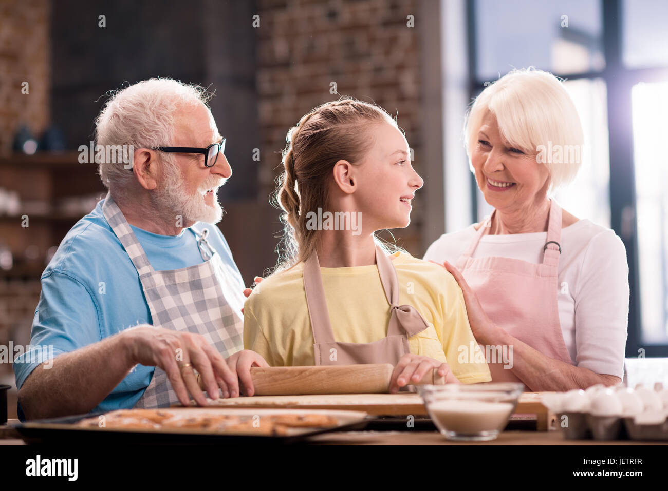 Grand-mère, grand-père et petite-fille de pétrissage et cuisson de la pâte pour les cookies avec des ustensiles de cuisine à la table de cuisine, la cuisson au concept de cuisine Banque D'Images