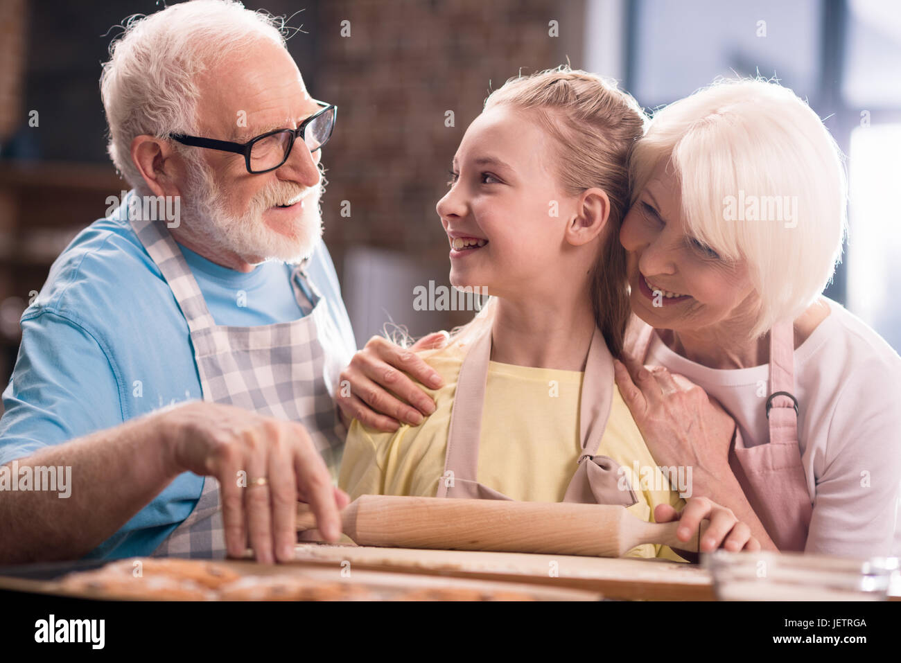 Grand-mère, grand-père et petite-fille de pétrissage et cuisson de la pâte pour les cookies avec des ustensiles de cuisine à la table de cuisine, la cuisson au concept de cuisine Banque D'Images