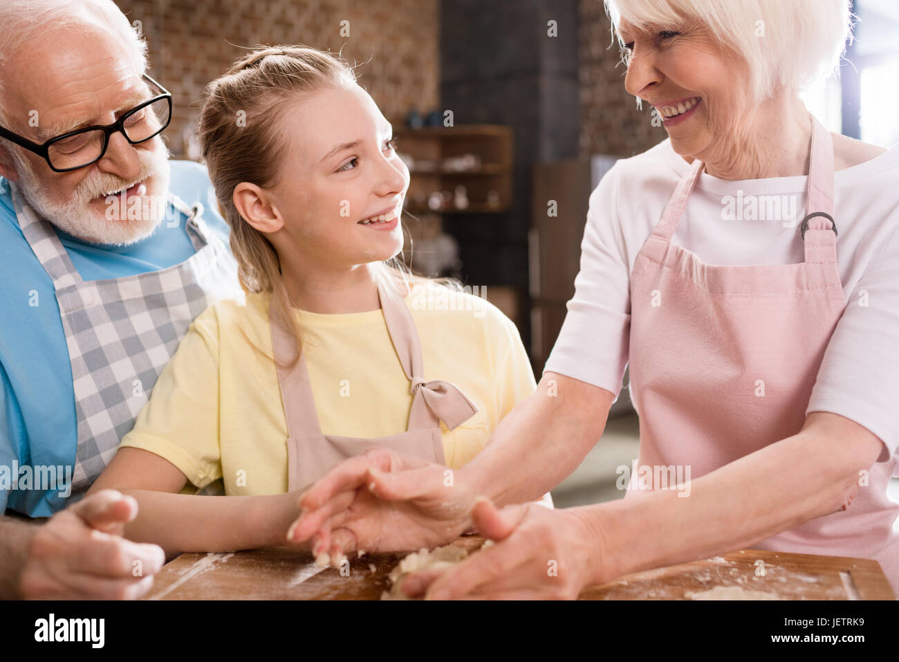 Grand-mère, grand-père et petite-fille de pétrissage et cuisson de la pâte pour les cookies à table de cuisine, la cuisson au concept de cuisine Banque D'Images