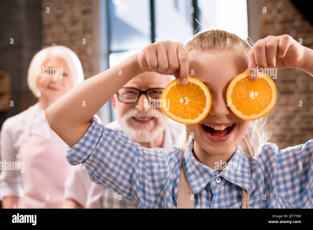Portrait of smiling girl holding fresh les tranches d'orange avec son grand-père derrière Banque D'Images